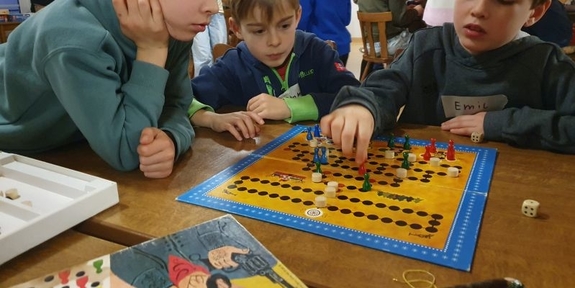Kinder sitzen an einem Tisch um ein Spielfeld herum