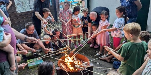 Kinder stehen um ein Lagerfeuer und halten Stockbrot darüber