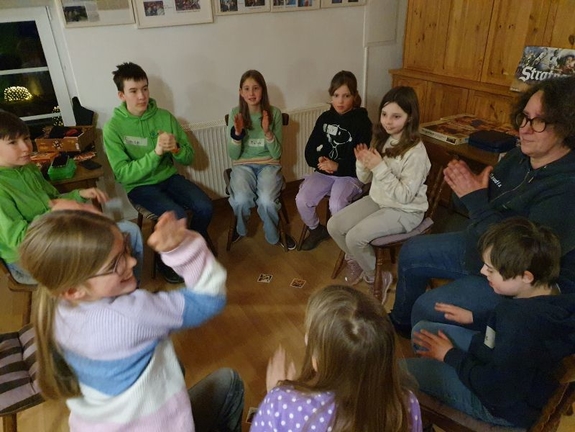 Gruppe sitzt im Kreis auf Stühlen und klatscht in die Hände